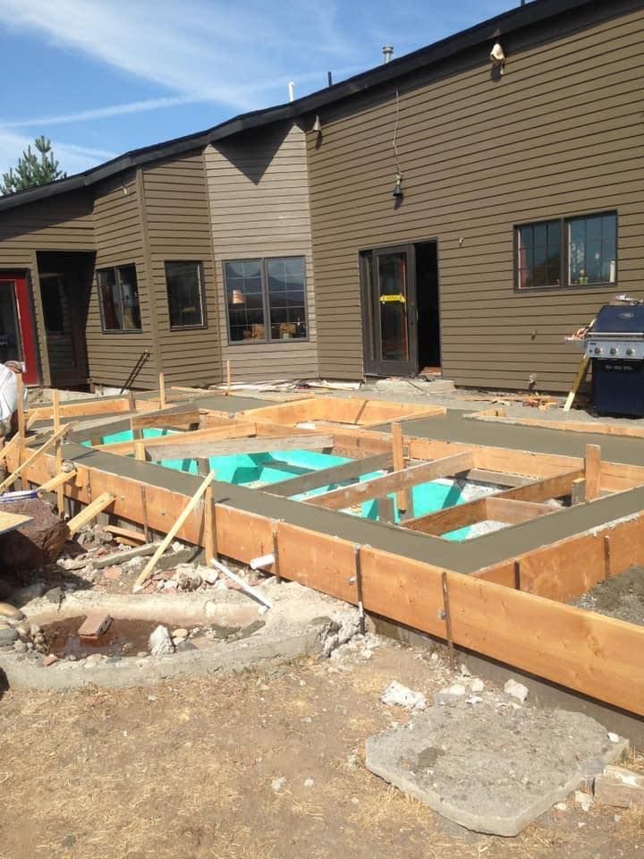 Concrete foundation being constructed outside a brown building, wood frames with blue insulation.