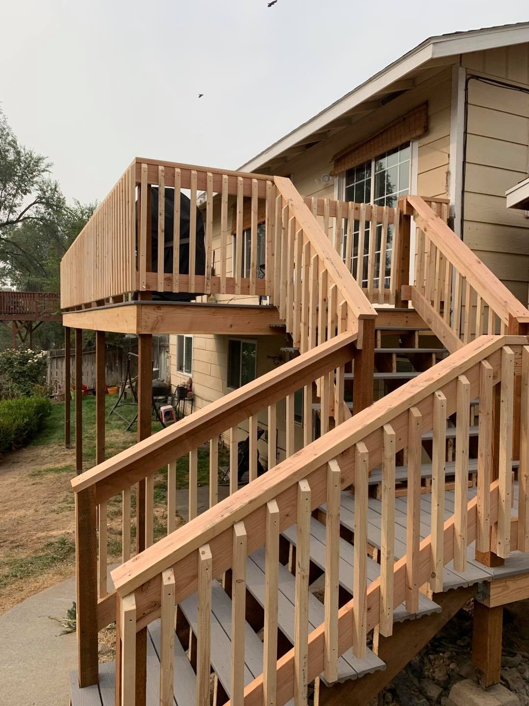 Wooden deck and staircase attached to a tan house. Clear sunny day.