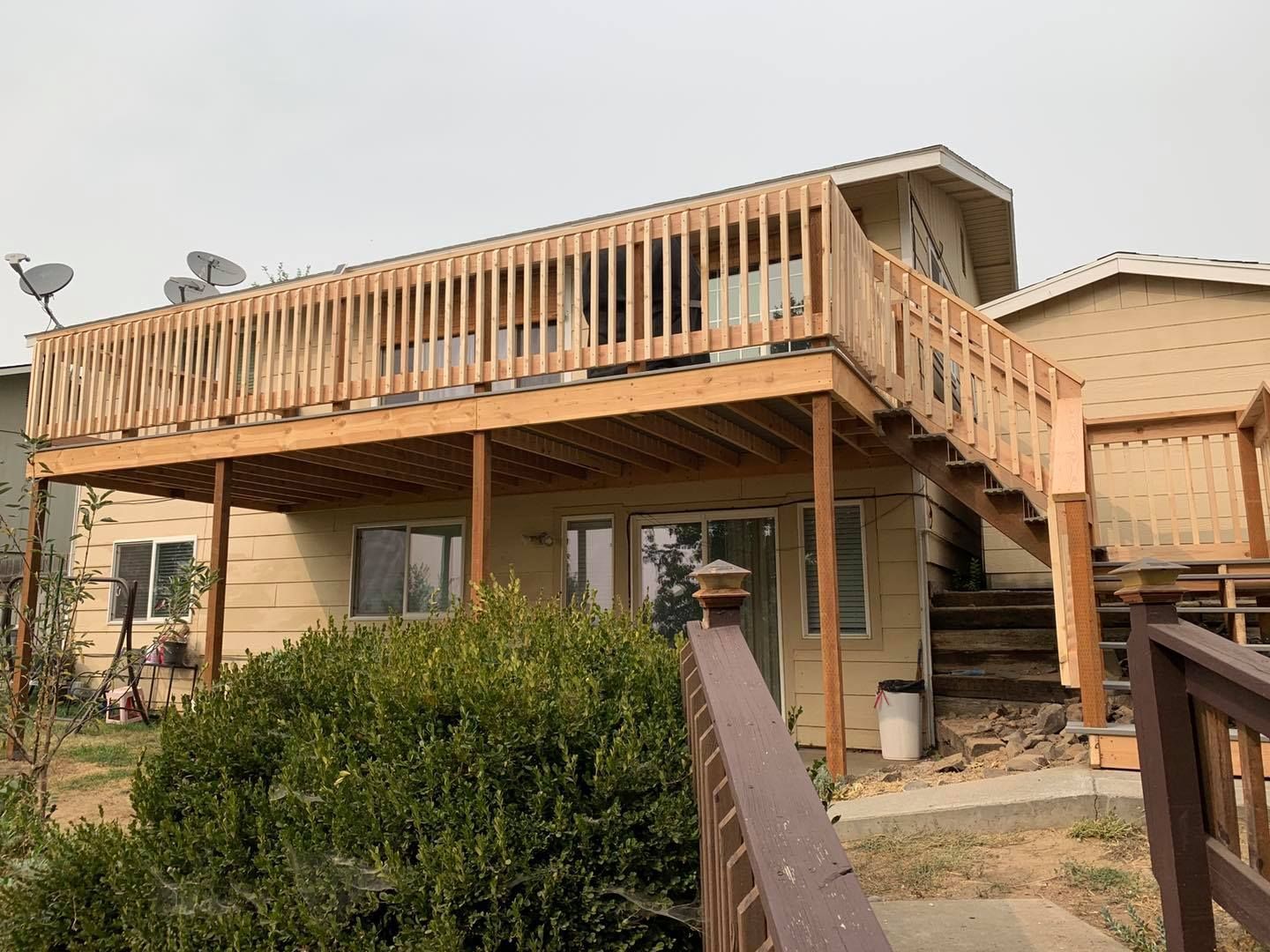 Two-story beige house with a wooden deck; stairs lead up. Overcast sky.