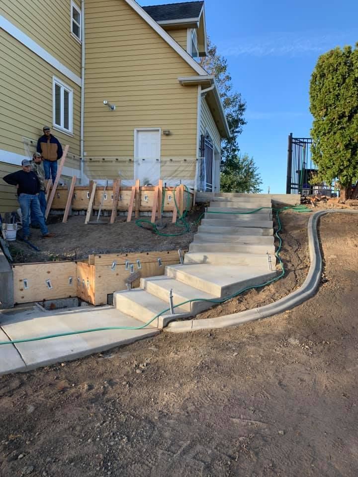Concrete steps being constructed next to a yellow house. Workers are on site.