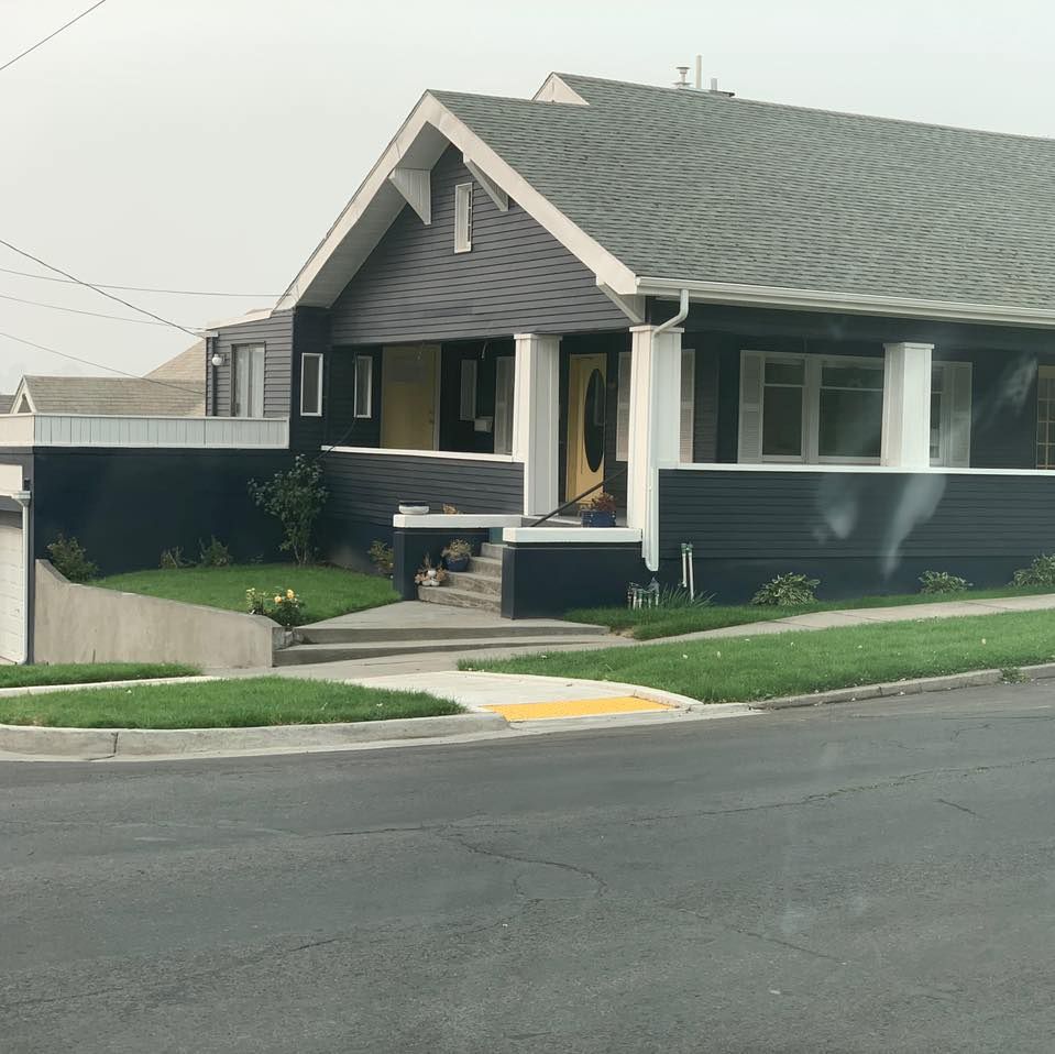 Dark gray Craftsman home with white trim, yellow door, and small front lawn.