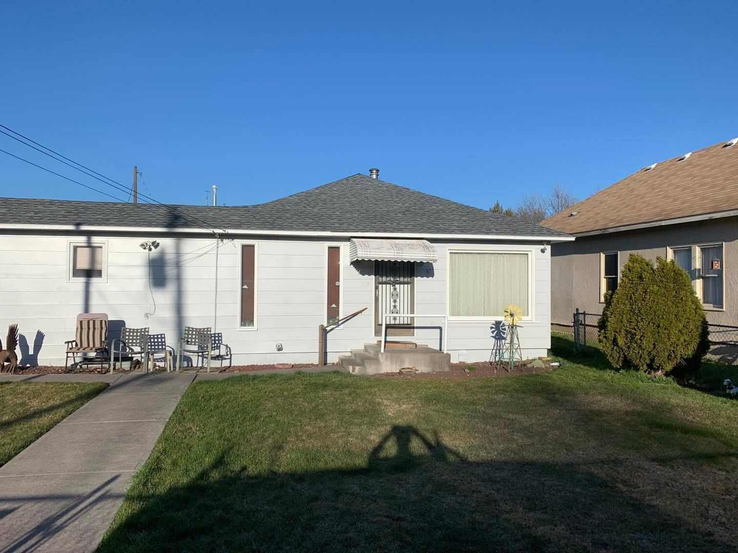 White single-story house with a small lawn, a sidewalk, and a neighbor's house to the right. Blue sky.
