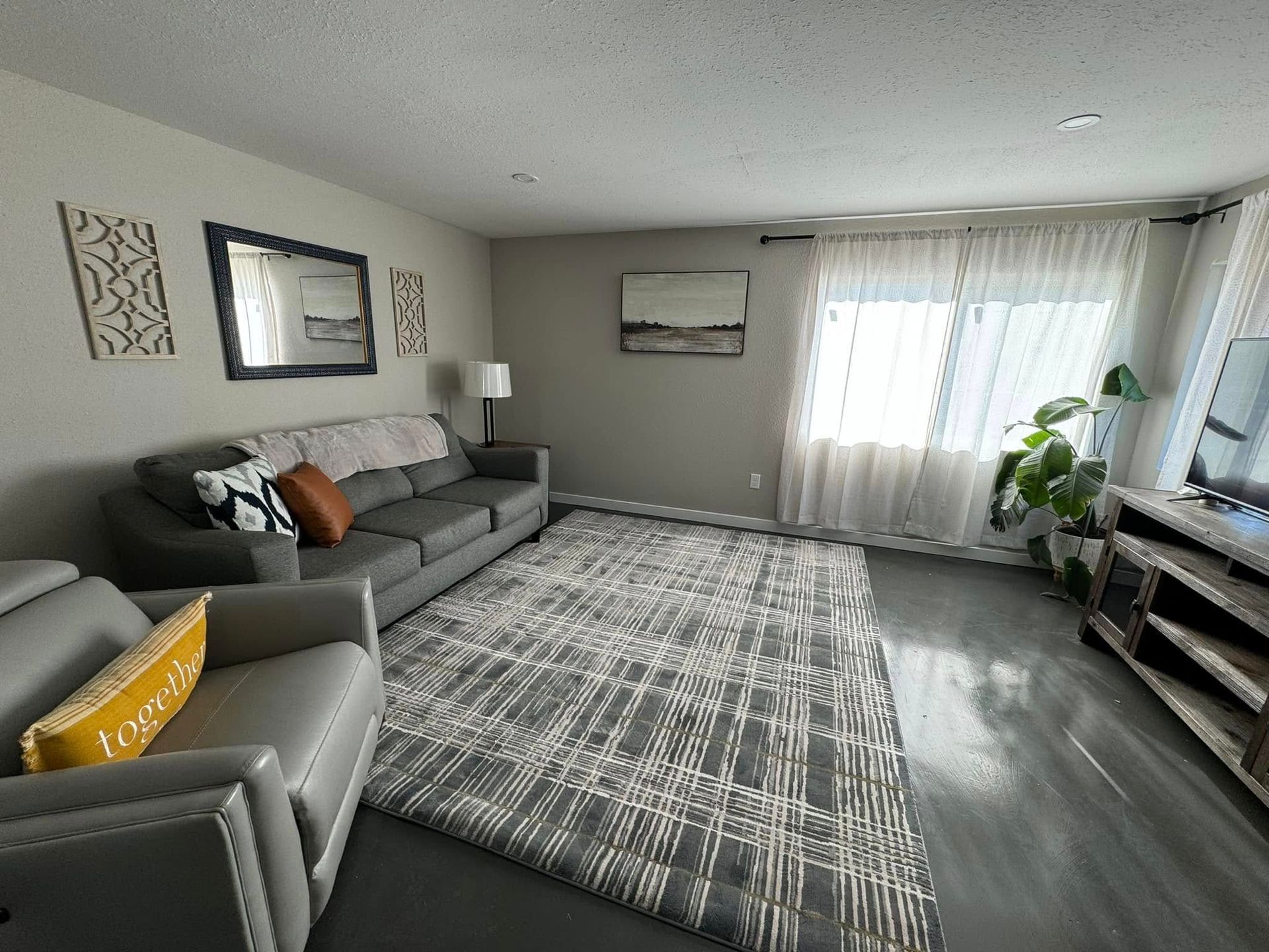 Living room with gray sofa, patterned rug, sheer curtains, and wooden entertainment center.