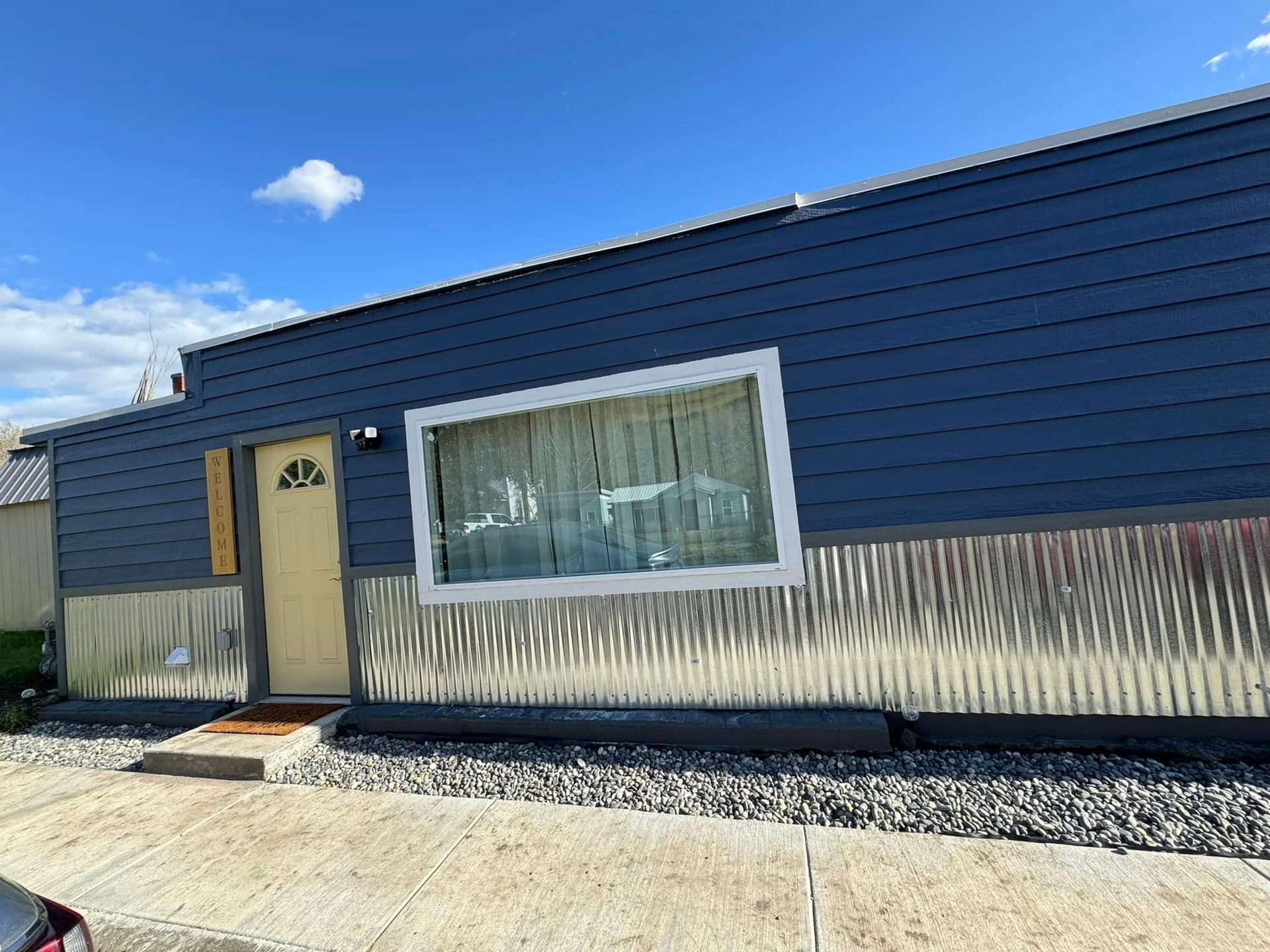 Blue and corrugated metal building exterior with door, window, and gravel landscaping.