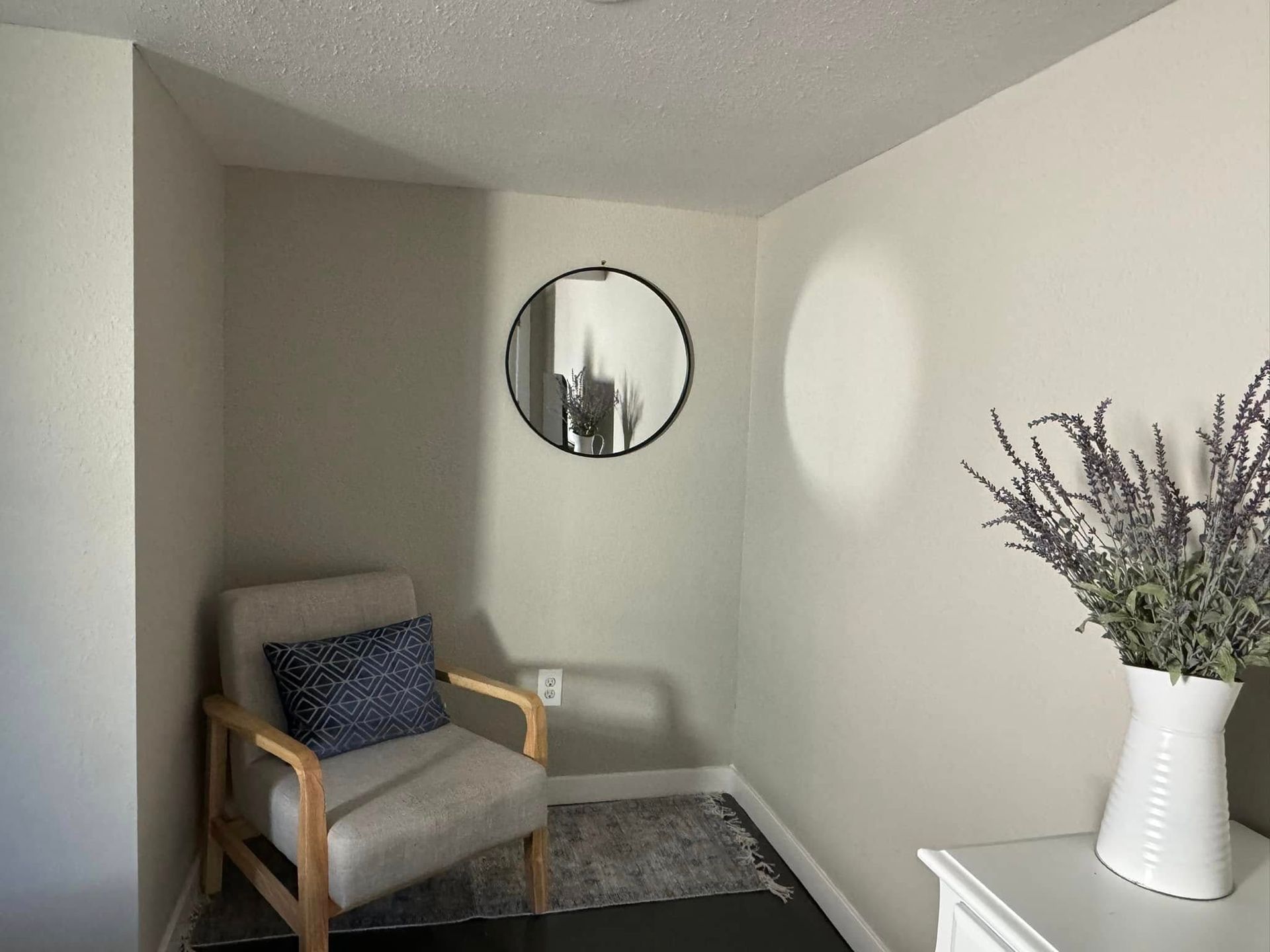 Small alcove with a chair, round mirror, and a vase of flowers.