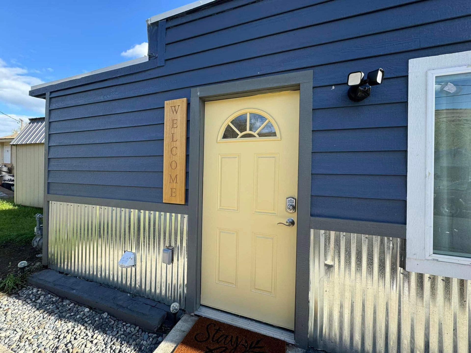 Blue tiny house with a yellow door, corrugated metal siding, and a