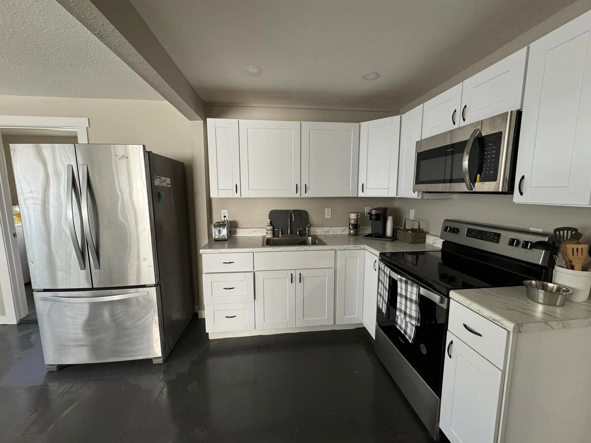 White kitchen with stainless steel appliances, white cabinets, and dark gray flooring.