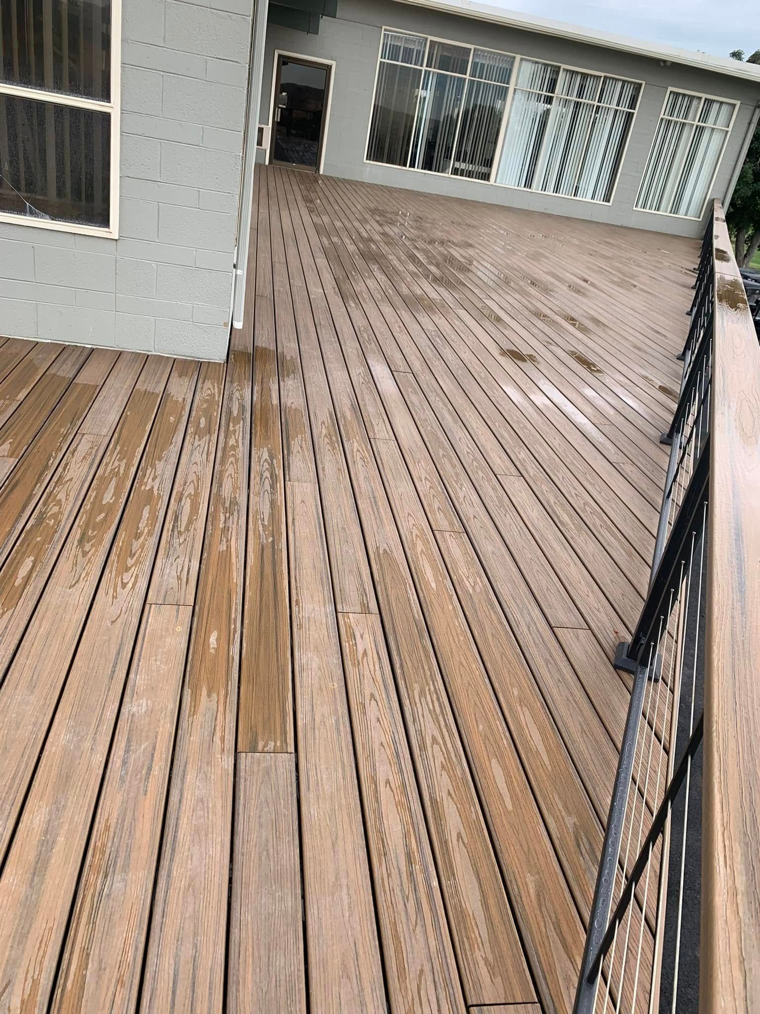 Wooden deck with metal railing next to a house with large windows.
