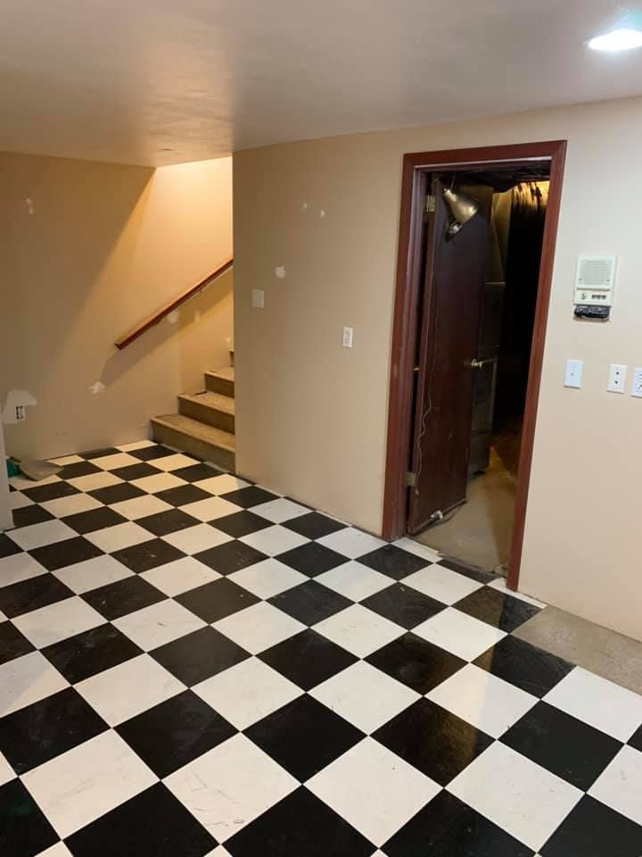 A room with black and white checkered floor, stairs, and a doorway. Beige walls and a brown door.