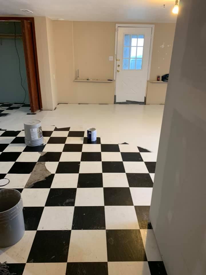 Black and white checkered tile floor being installed in a room with white and beige walls; a white door is visible.