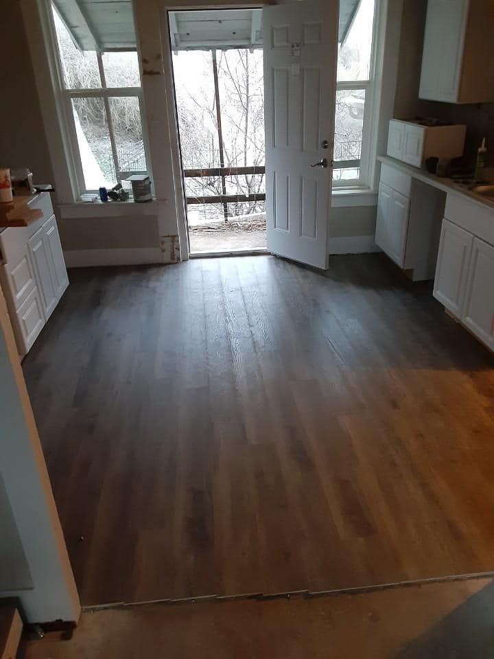 Kitchen with newly installed dark wood flooring, white cabinets, and a doorway leading outside.