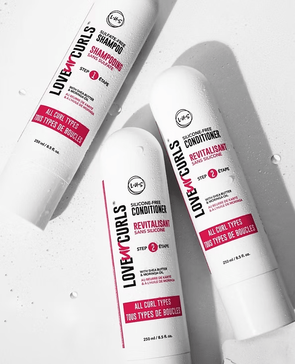 Three white bottles of "Love By Curls" shampoo and conditioner on a white surface, with pink labels.