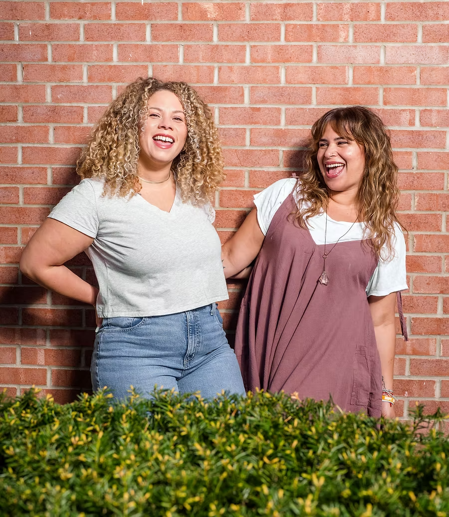 Woman with curly, blonde-brown hair, wearing an orange top and looking away.