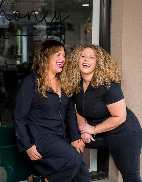 Woman with curly, blonde-brown hair, wearing an orange top and looking away.