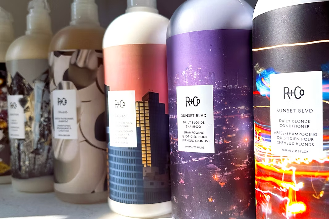 Row of colorful R+Co shampoo bottles with cityscape designs.