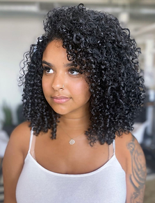 Woman with dark curly hair and a white tank top looking off to the side.