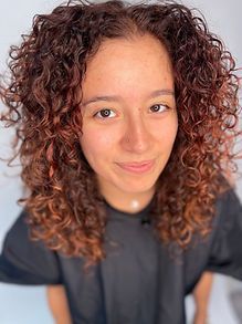 Woman with curly auburn hair, smiling, wearing a dark shirt.