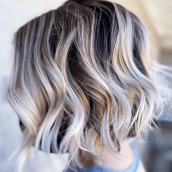 Wavy, short hair styled with dark roots fading to light blonde and gray highlights.