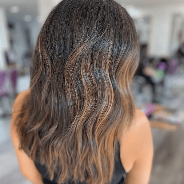 Woman with wavy brown hair, sun-kissed highlights, in a salon setting.