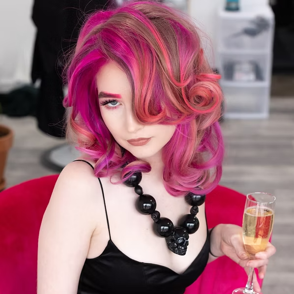 Woman with pink hair and black dress holding champagne, wearing a skull necklace.