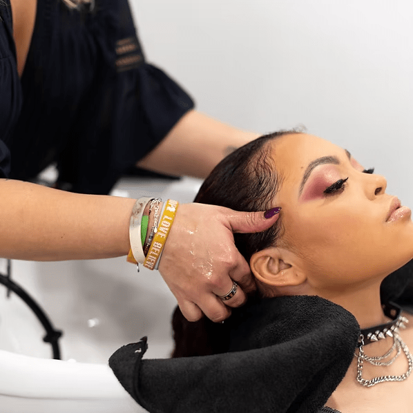 Person getting hair washed at salon; stylist's hands massaging scalp.