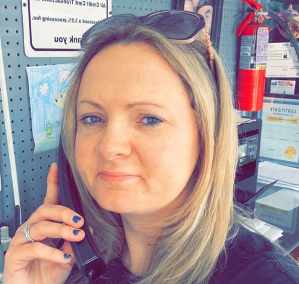 Woman with blonde hair, on the phone, wearing sunglasses on head, indoors, near a fire extinguisher.