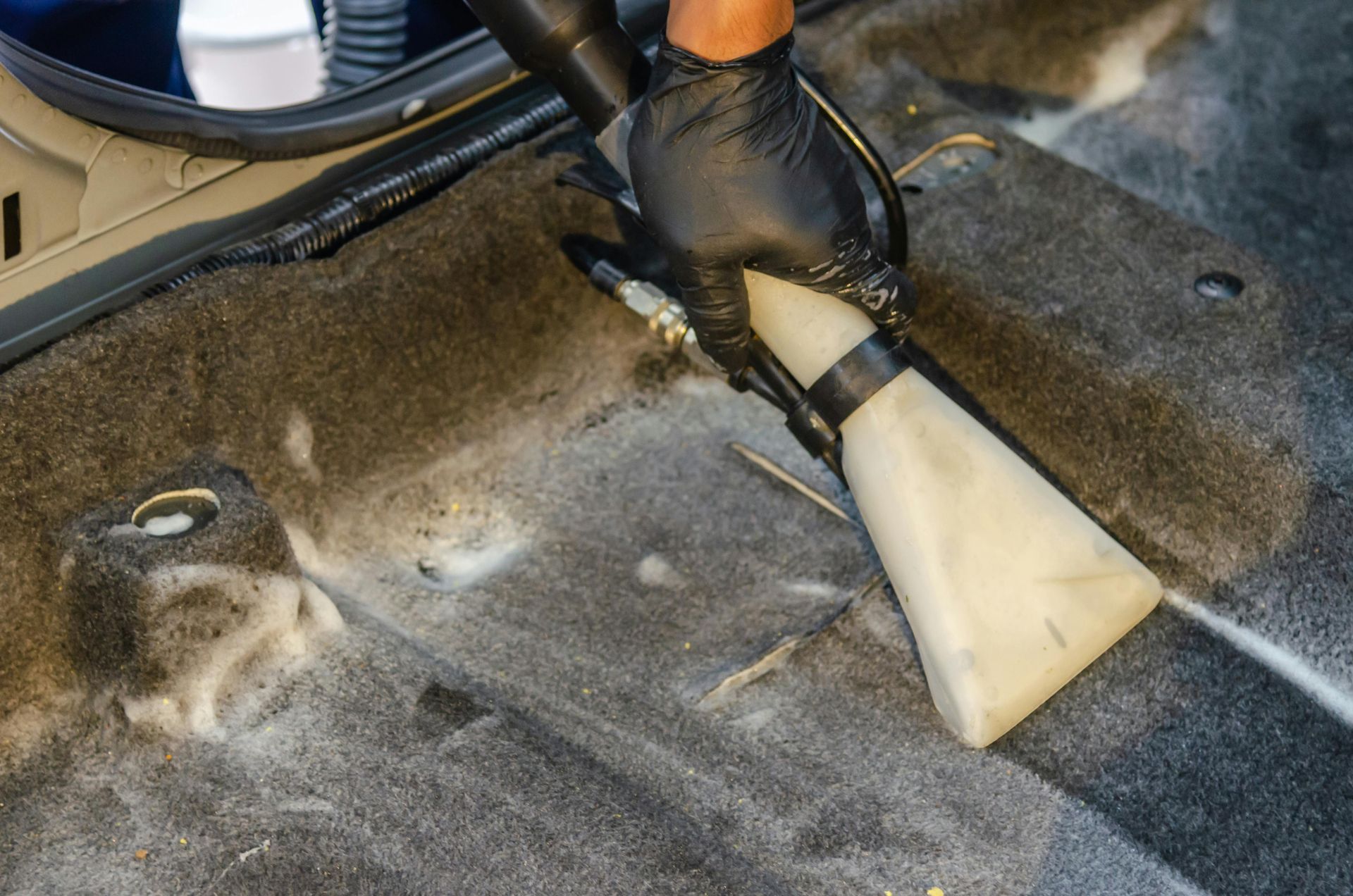 Person in black gloves vacuuming a car's dirty floor.