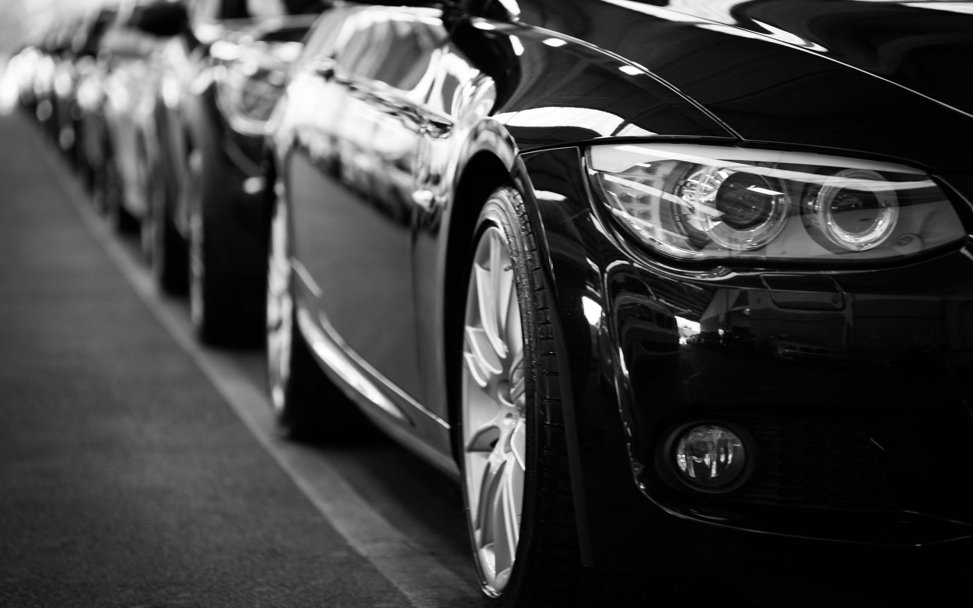 Row of black cars parked in a line, close-up of the front of a car with a shiny surface.