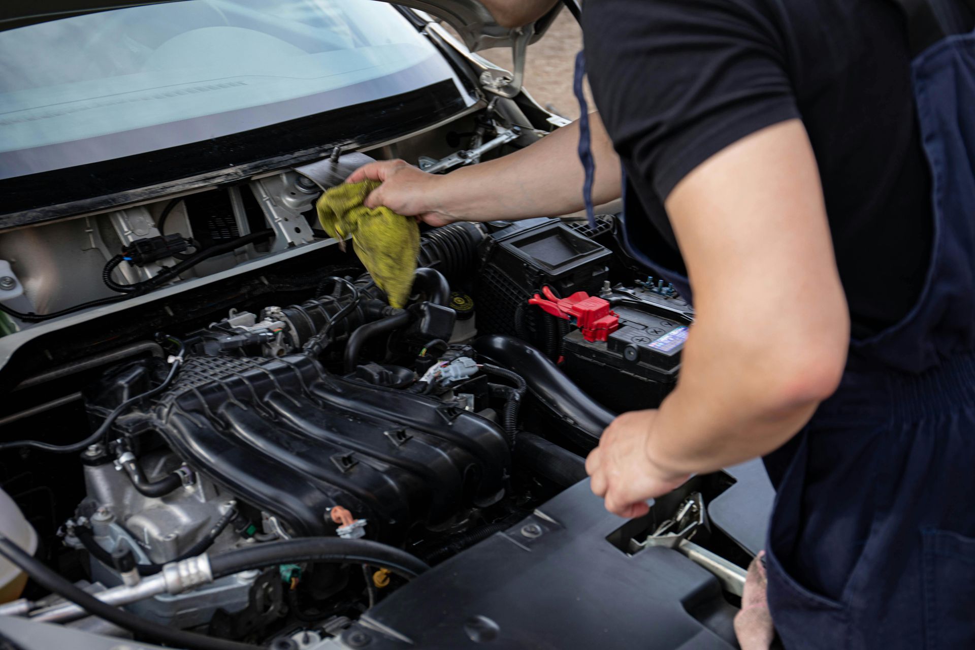 Mechanic cleaning car engine bay with a yellow cloth.