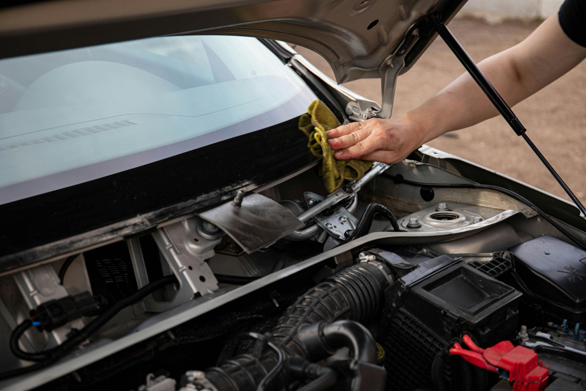 Person cleaning a car engine bay with a yellow cloth.