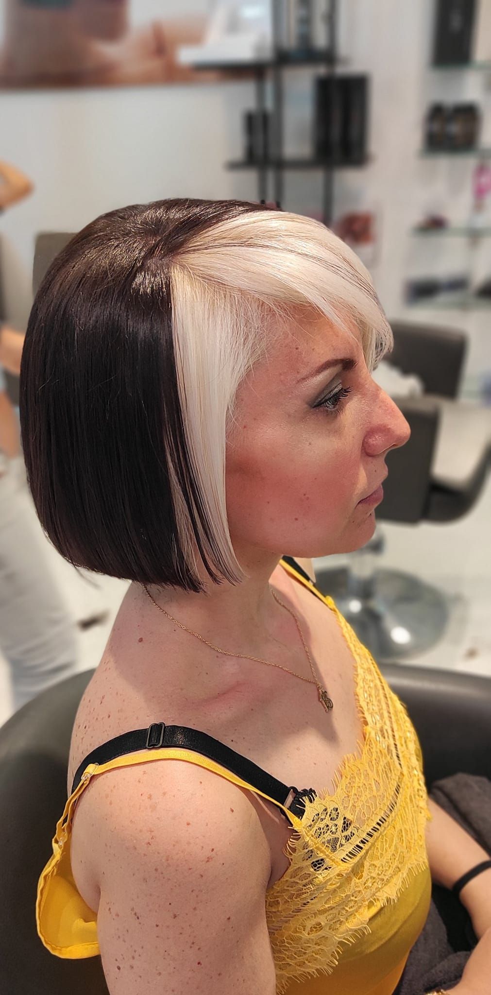 Una donna con una canottiera gialla si sta tingendo i capelli in un salone.