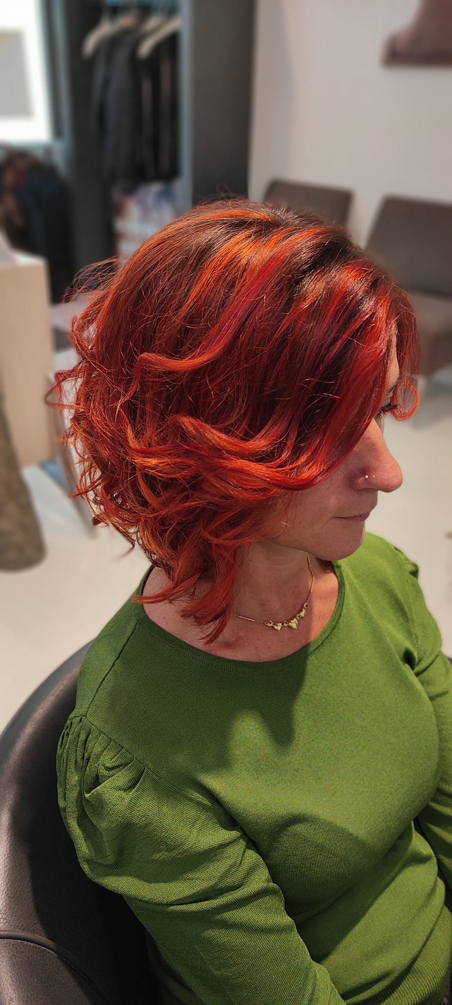 Una donna con i capelli rossi indossa un maglione verde ed è seduta su una sedia.
