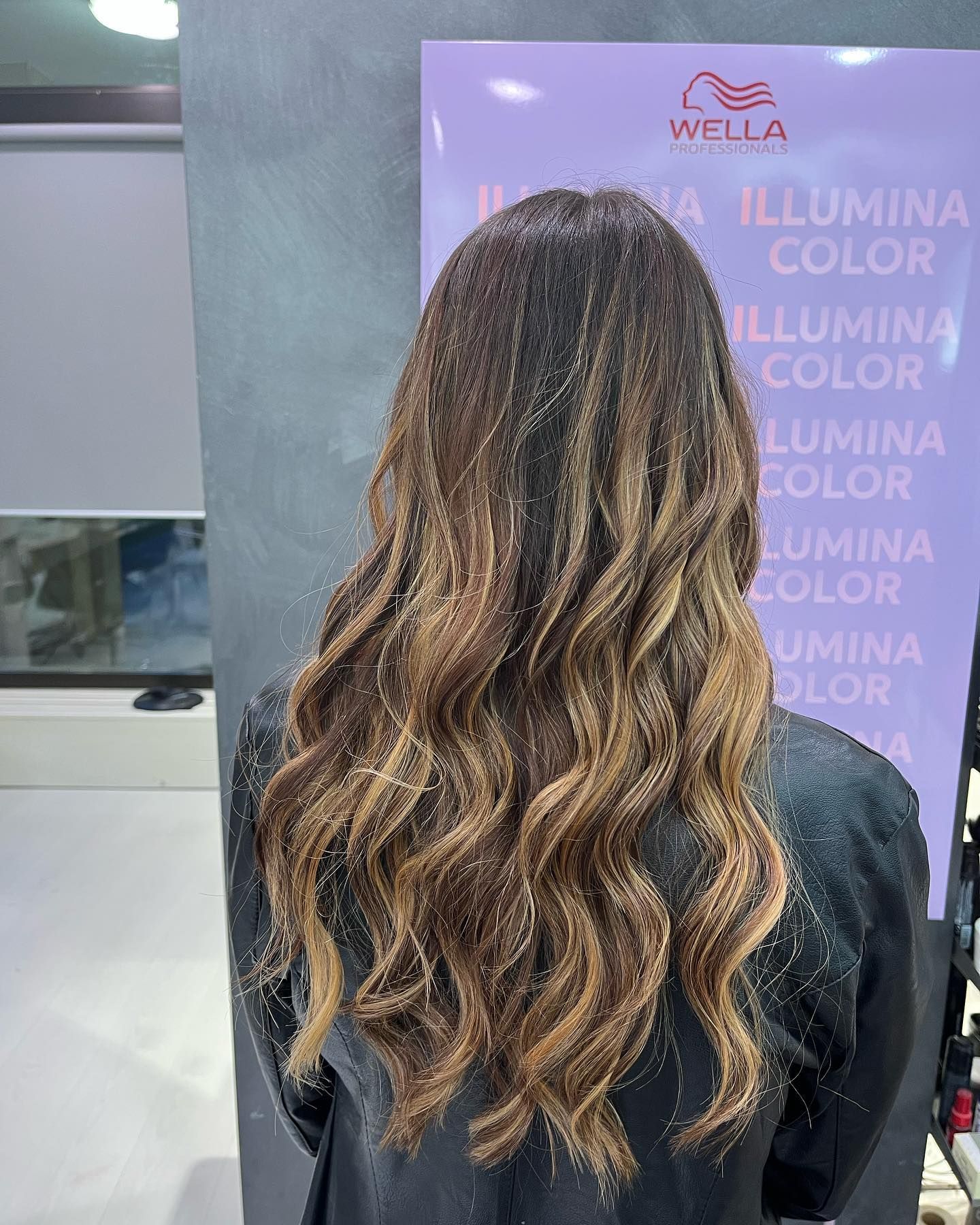 Una donna con lunghi capelli castani è in piedi davanti a un cartello Wella.