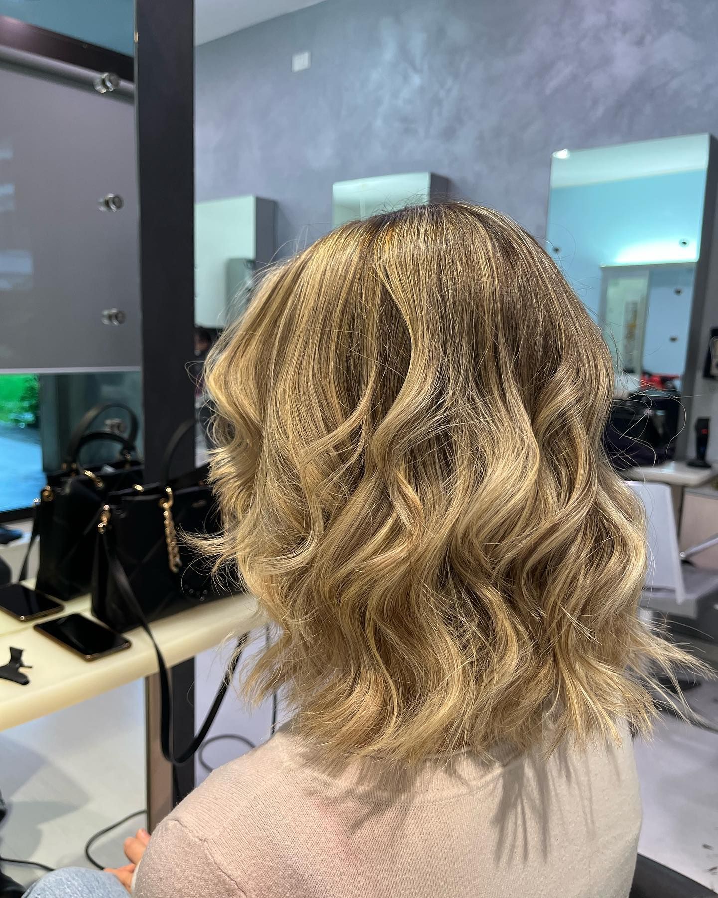 Una donna con i capelli biondi è seduta davanti allo specchio in un salone.