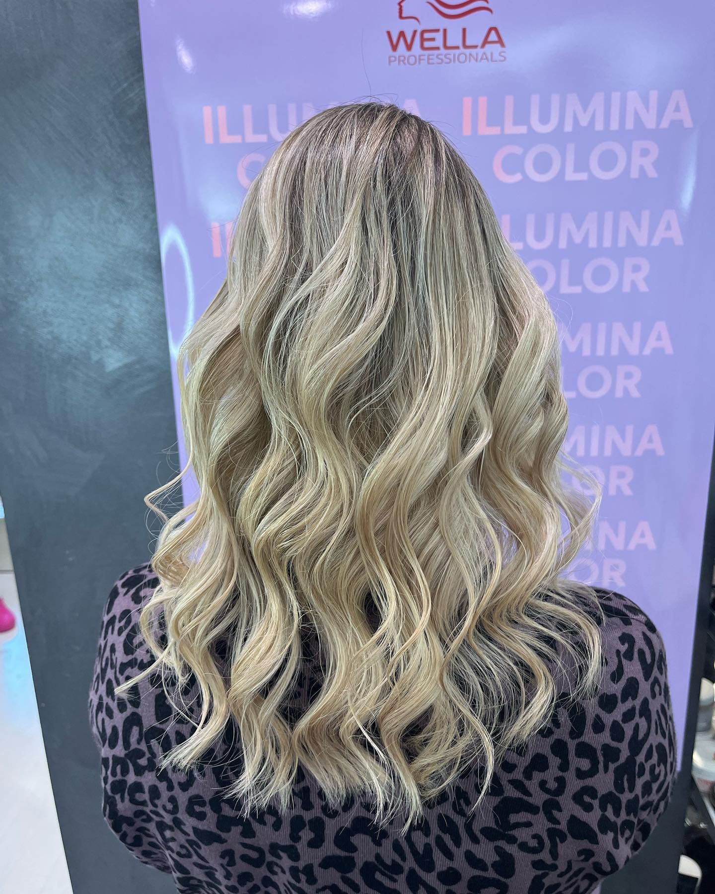 Una donna con lunghi capelli biondi è in piedi davanti a un cartello Wella.