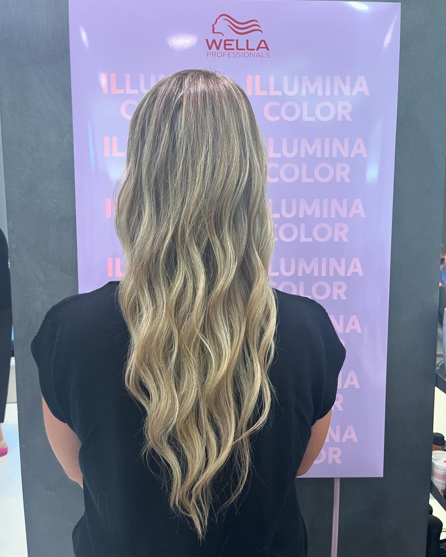 Una donna con lunghi capelli biondi è in piedi davanti a un cartello Wella.