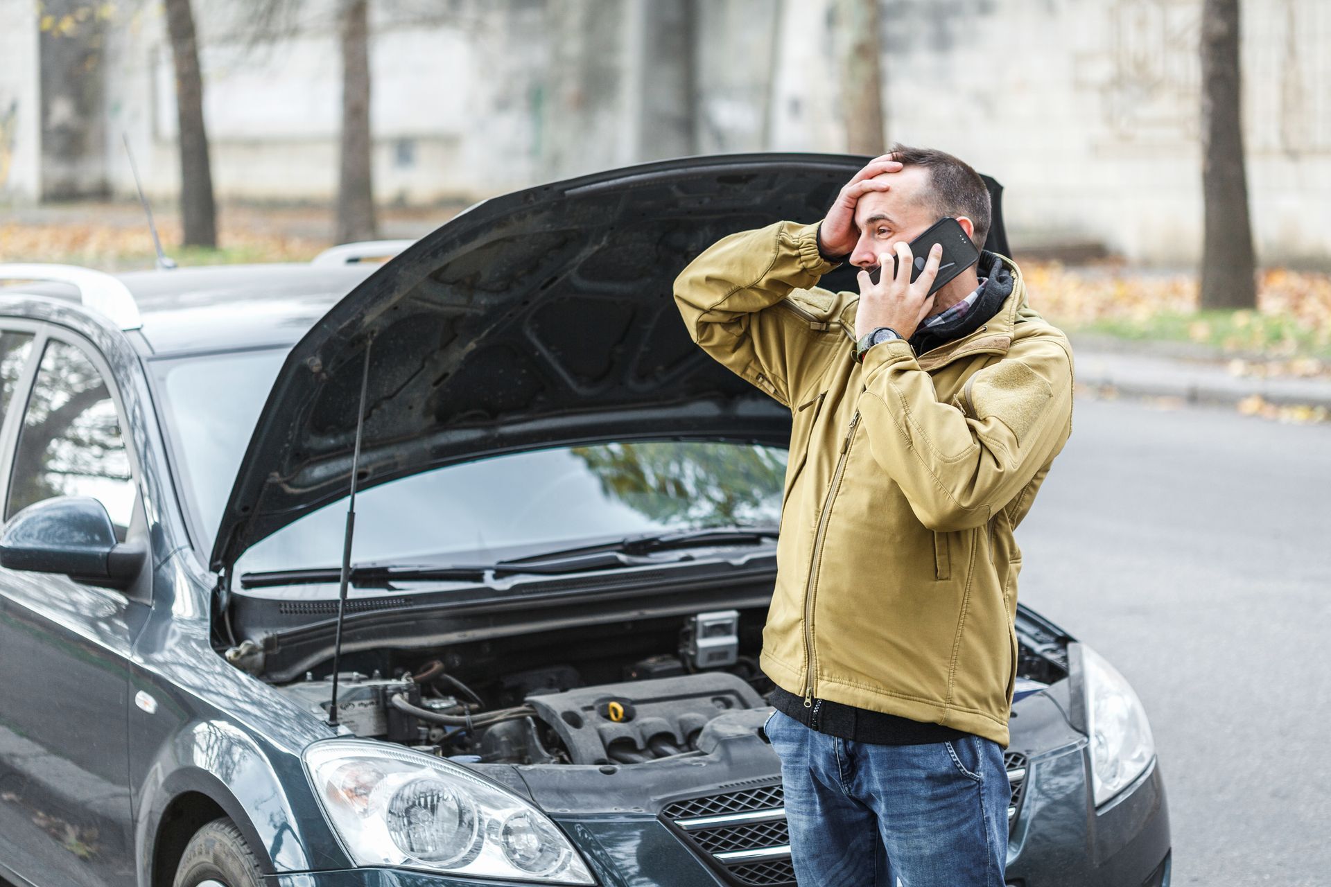 A man is talking on a cell phone in front of a broken down car.