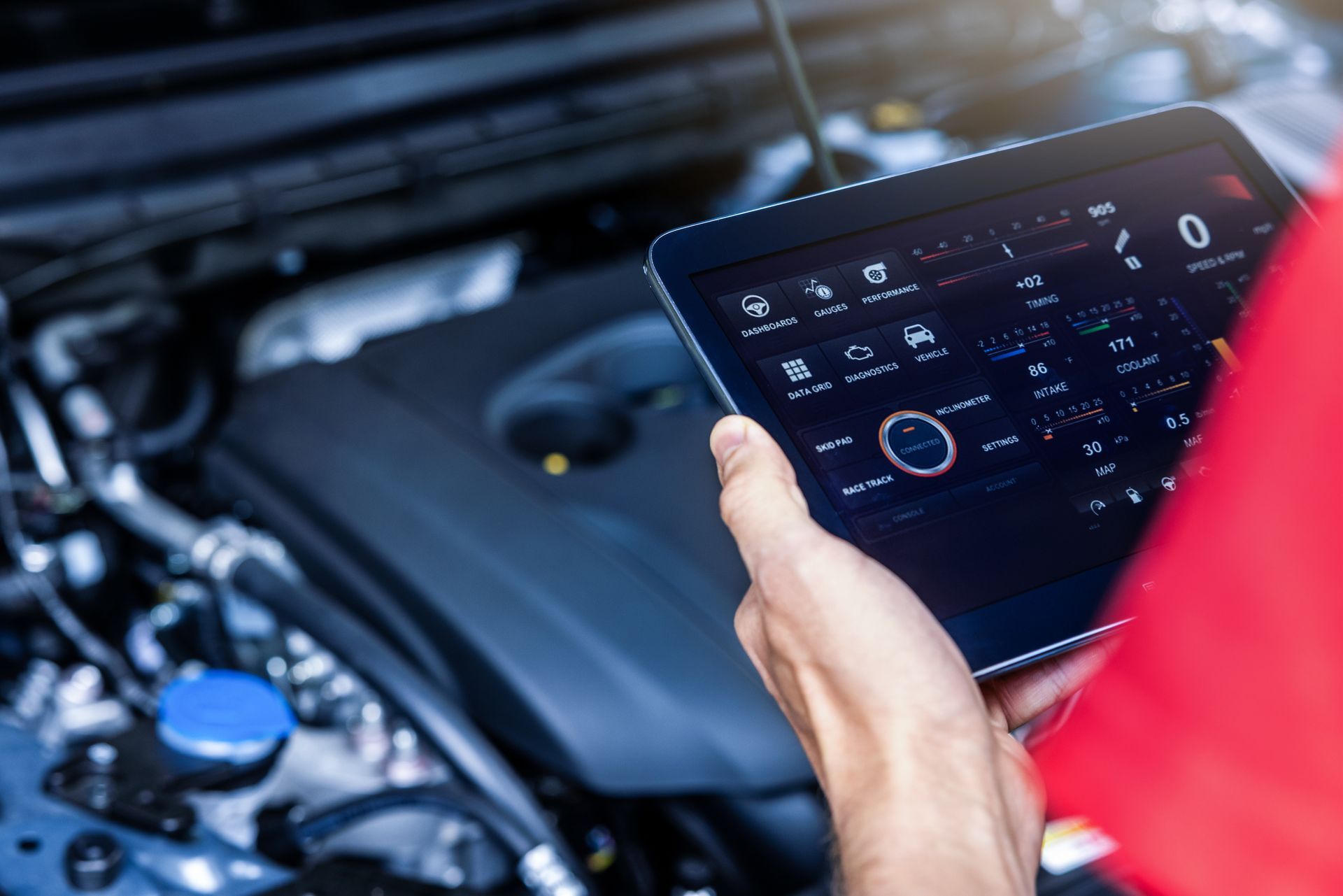 A person is holding a tablet in front of a car engine.