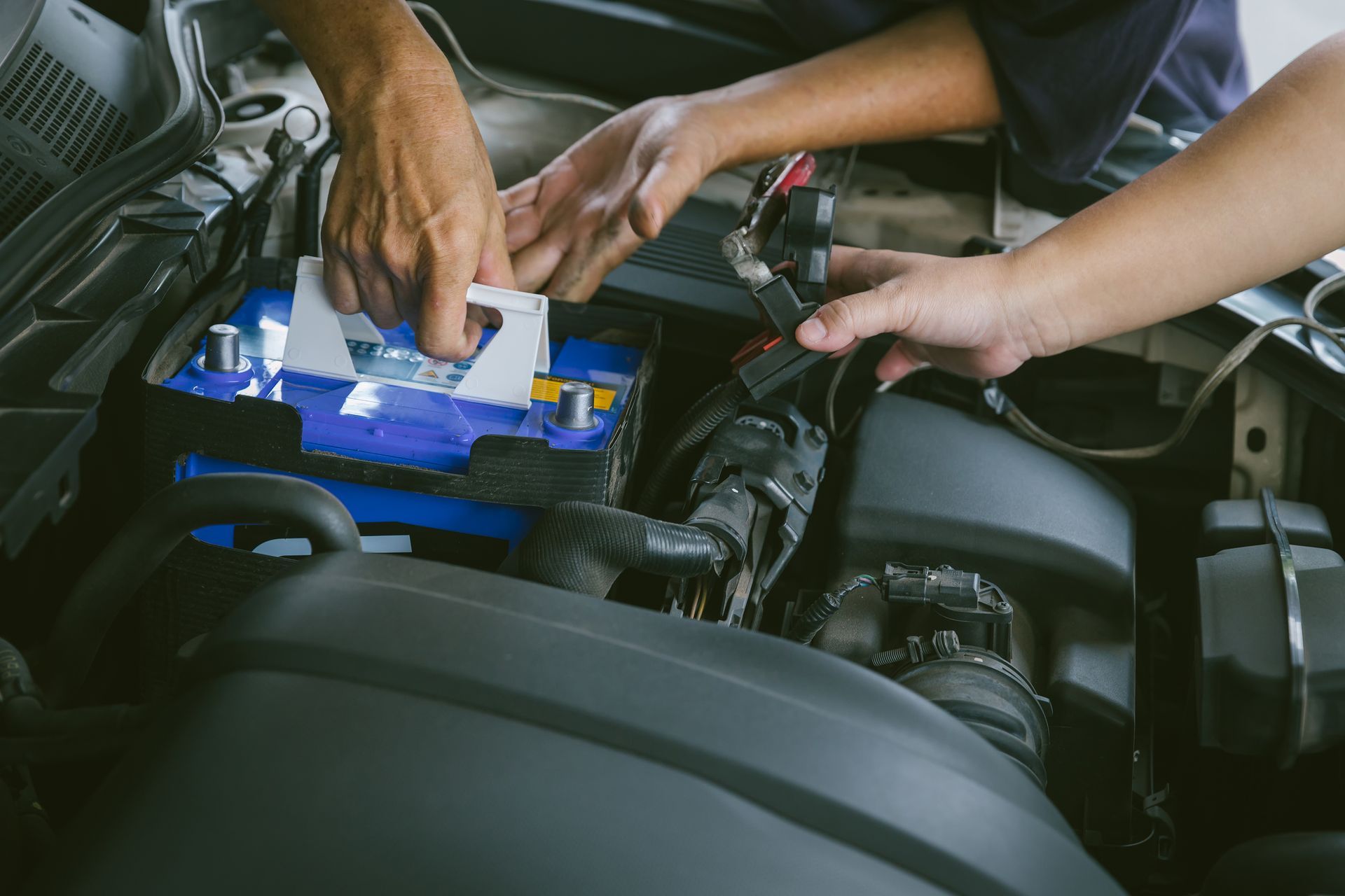 A man and a woman are working on a car battery.