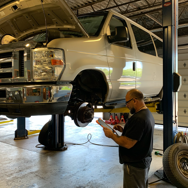 A man is standing next to a white van on a lift in a garage.