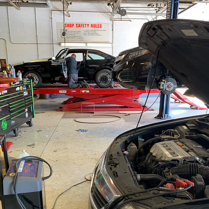 A man is working on a car in a garage with the hood open.