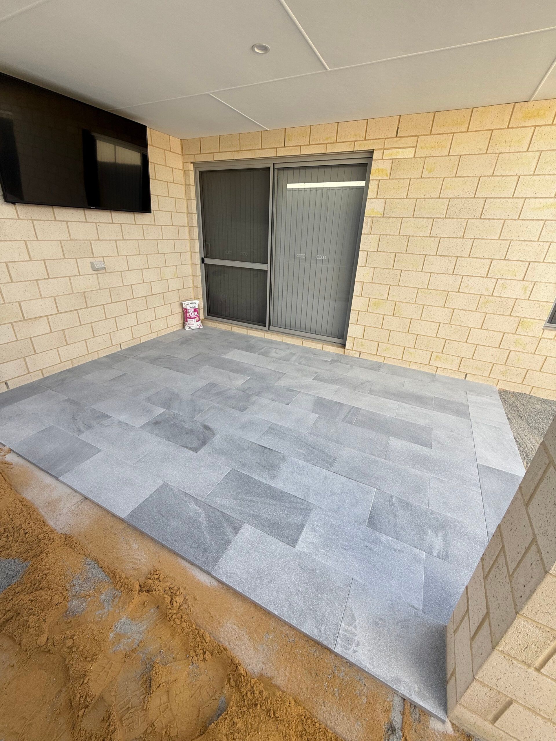 A patio with gray stone pavers next to a sliding glass door and light-colored brick walls.