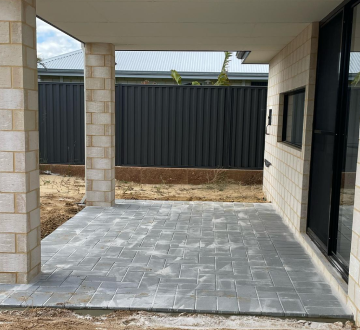 A newly paved grey herringbone patio under a covered porch with light-colored brick pillars and walls.