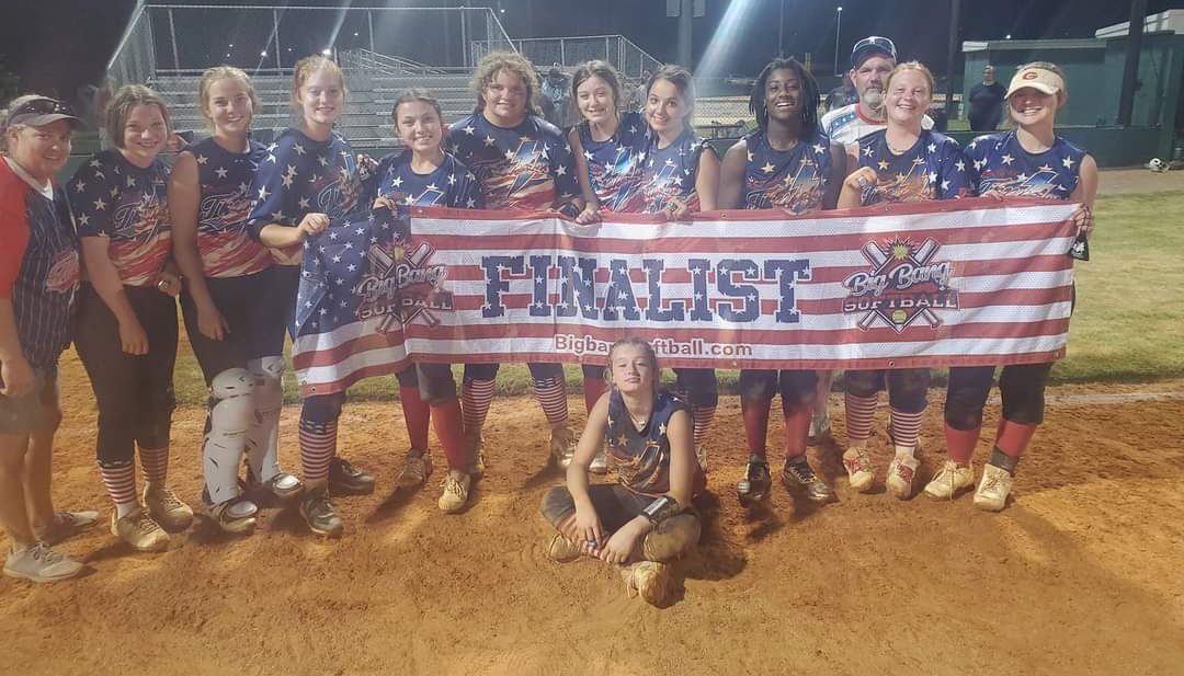 A softball team is posing for a picture while holding an american flag.