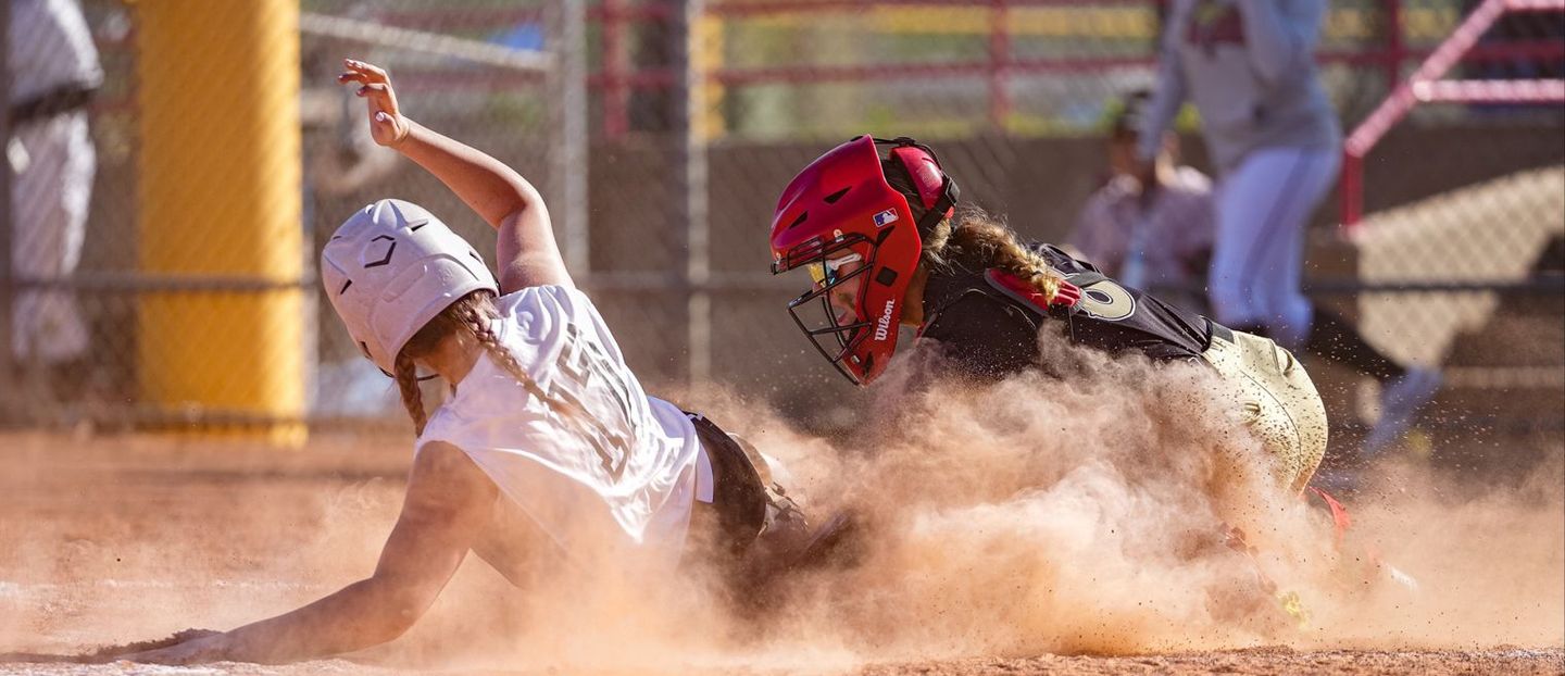 A girl is sliding into home plate during a softball game.