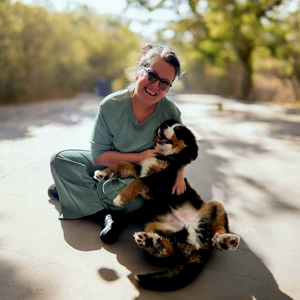 Woman in green outfit smiling, holding a Bernese Mountain Dog puppy on a sunny path. Woman in green outfit smiling, holding a Bernese Mountain Dog puppy on a sunny path.