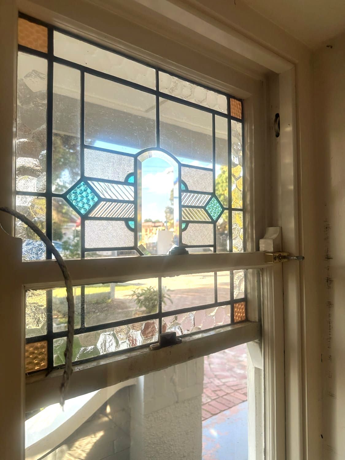 Stained glass window with blue, orange, and clear panes, set in a white frame, overlooking a street.