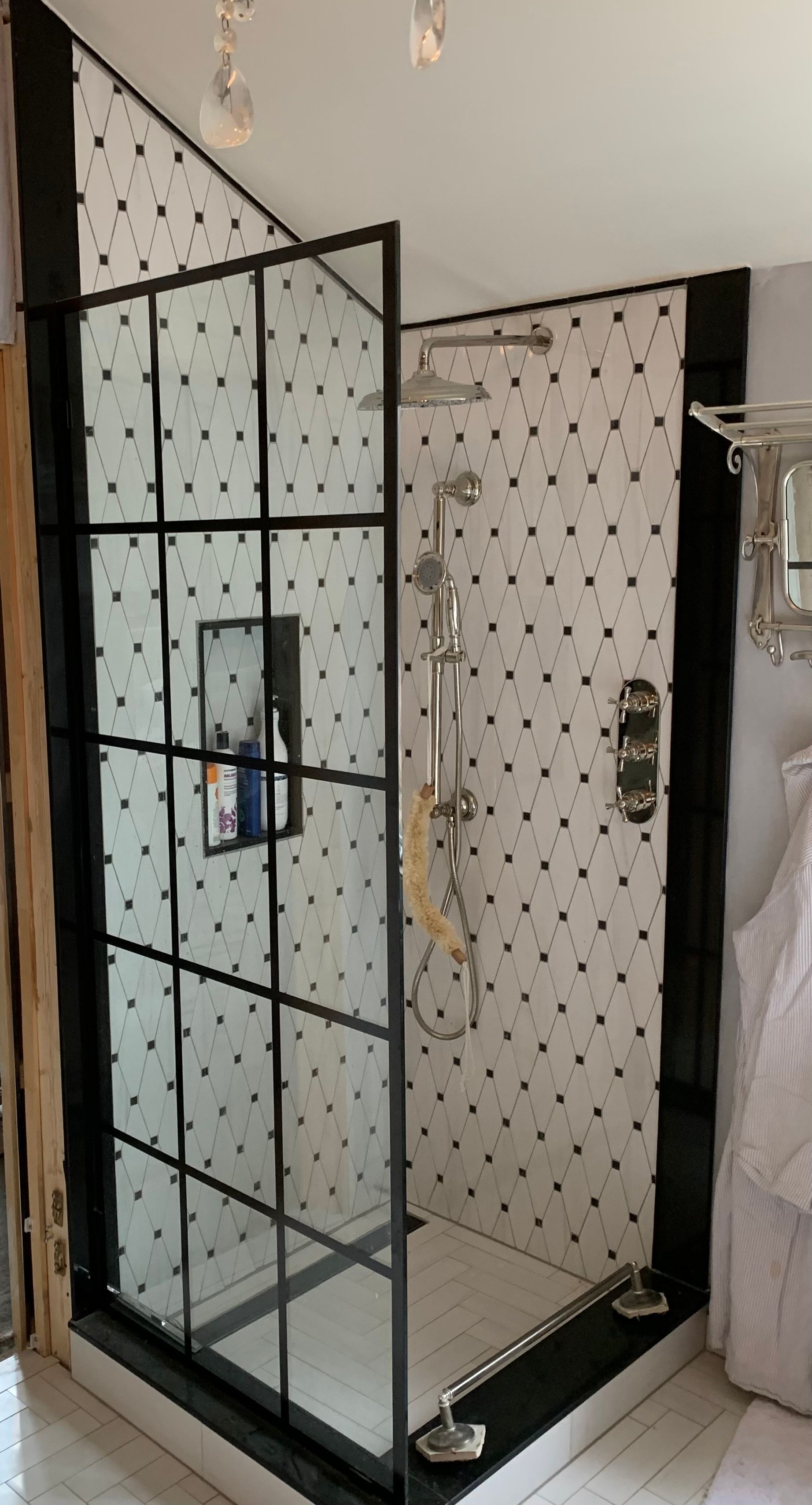 Black-framed shower with glass door and black and white tiled walls.