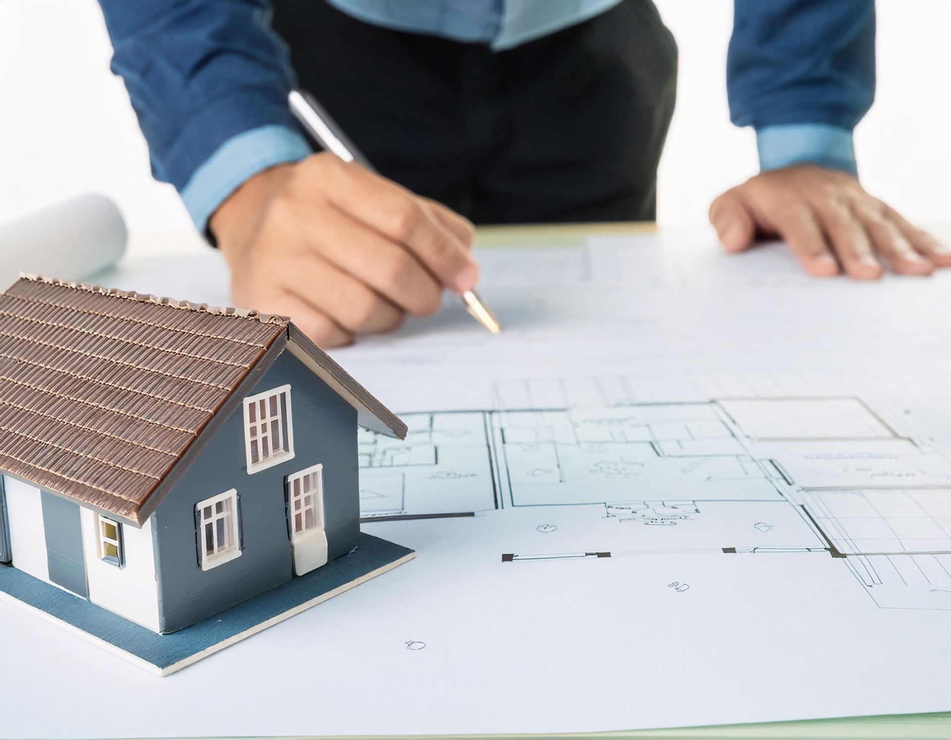 Architect working on blueprints, small house model, white surface, indoors.