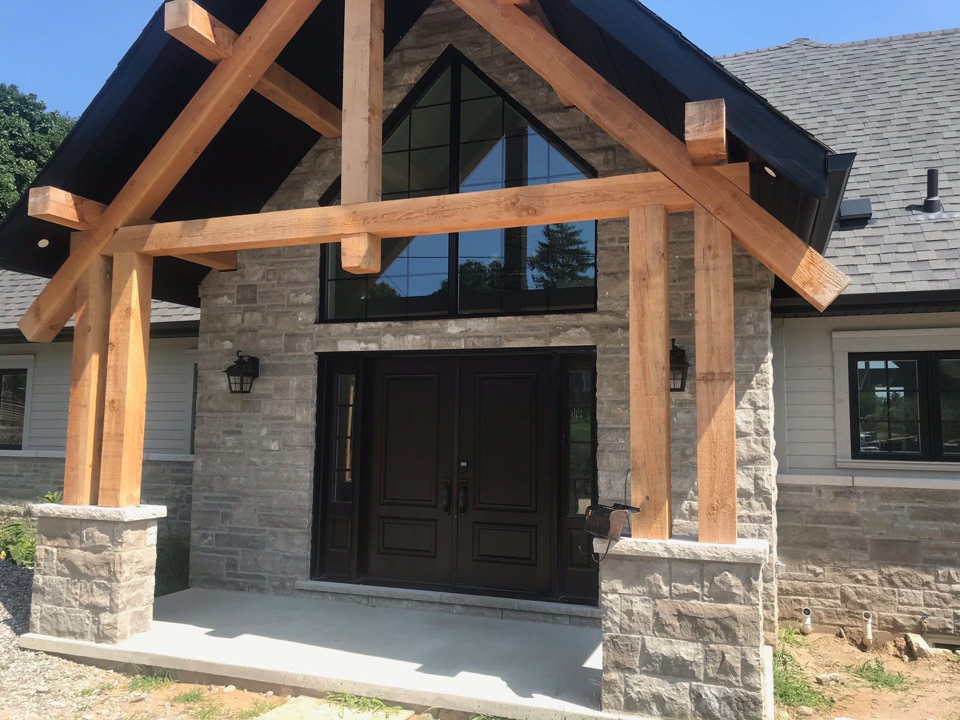 Stone-faced entrance with wooden beams over black double doors and a triangular window.